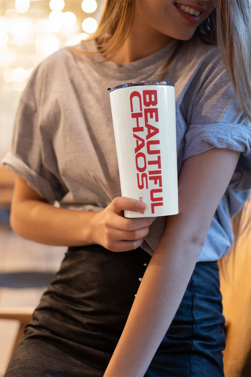 smiling model holding white katseye bottle with red beautiful chaos lettering
